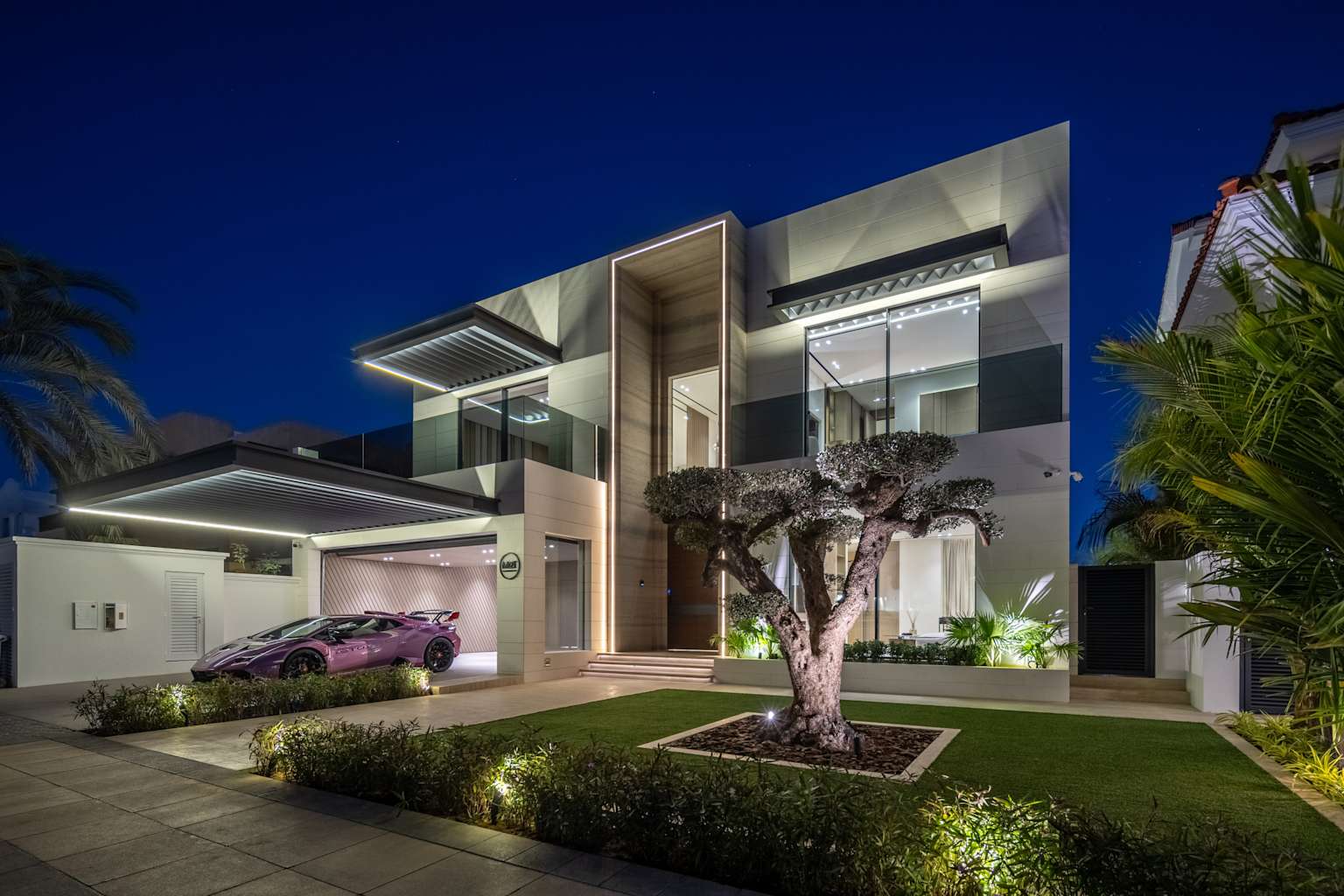 An illuminated contemporary luxury villa in Dubai featuring modern architecture and a high-performance sports car