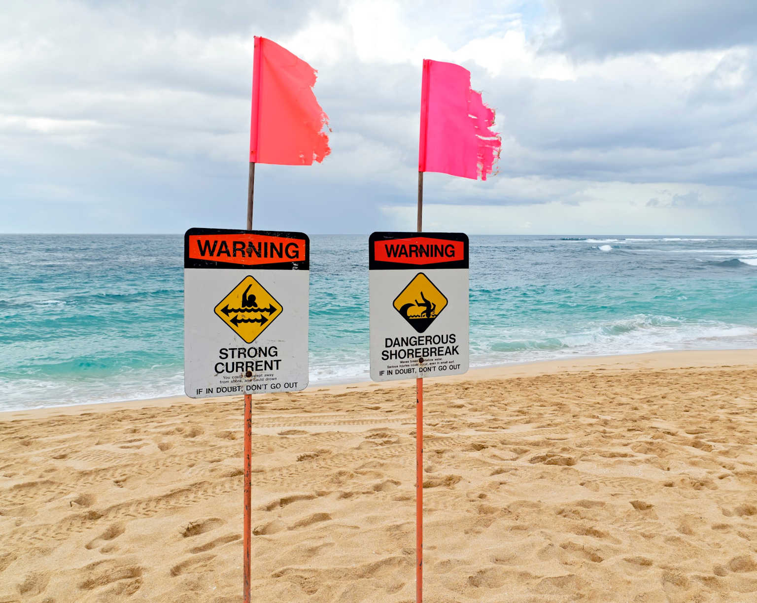 Warning signs on a Hawaii beach caution visitors about strong currents and dangerous shorebreaks advising them to avoid entering the water if unsure