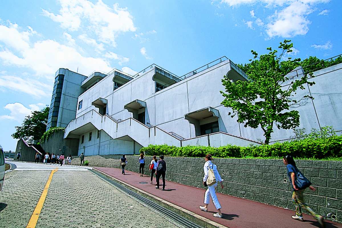 Exterior view of Tama Art University's Hachioji campus building with people walking nearby on a sunny day