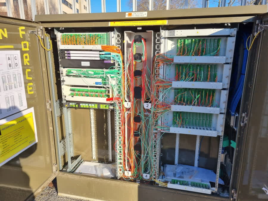 Open fiber optic distribution cabinet (PMZ) showing organized fiber optic patch panels and cables for network connection and maintenance