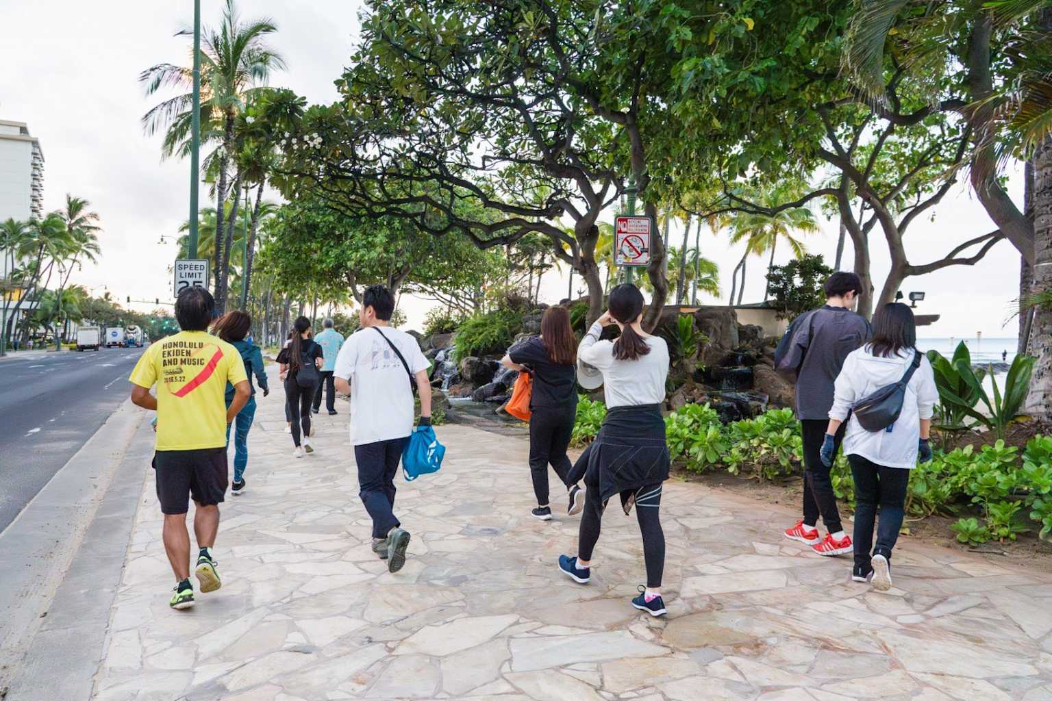 Tourists walking along a scenic Waikiki sidewalk surrounded by tropical greenery and palm trees, showcasing walking as a viable alternative to renting a car in Hawaii