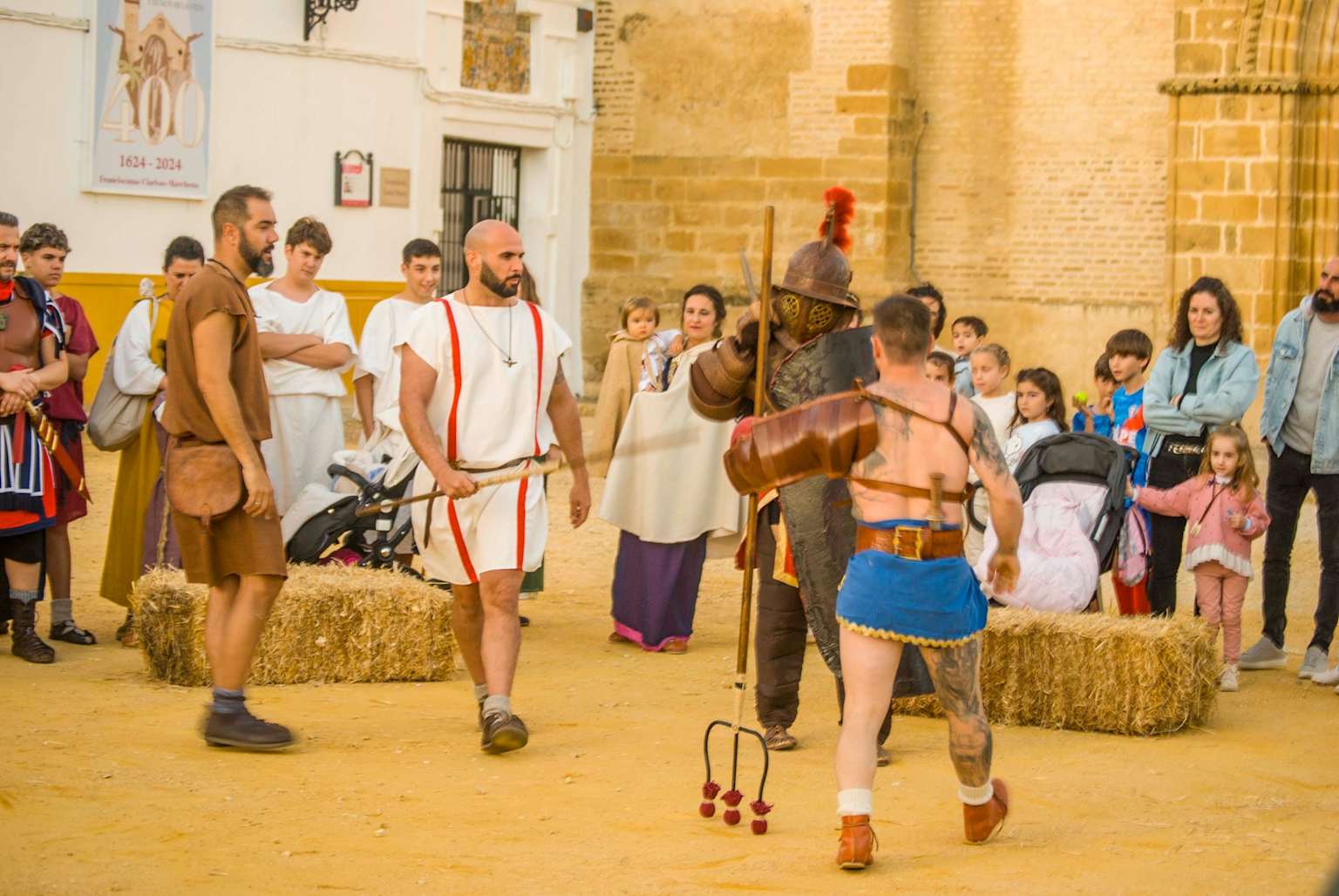 Recreadores históricos en un evento al aire libre, vestidos con trajes y armaduras de época, rodeados de público interesado
