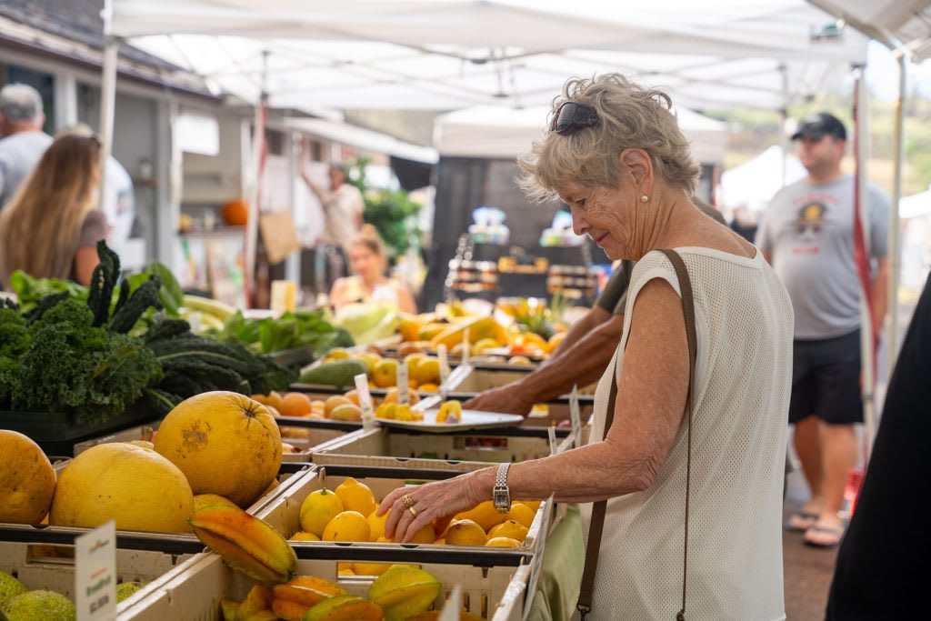 A local shopper explores fresh fruits and vegetables at a Hawaiian farmers market, highlighting affordable and fresh food options for locals