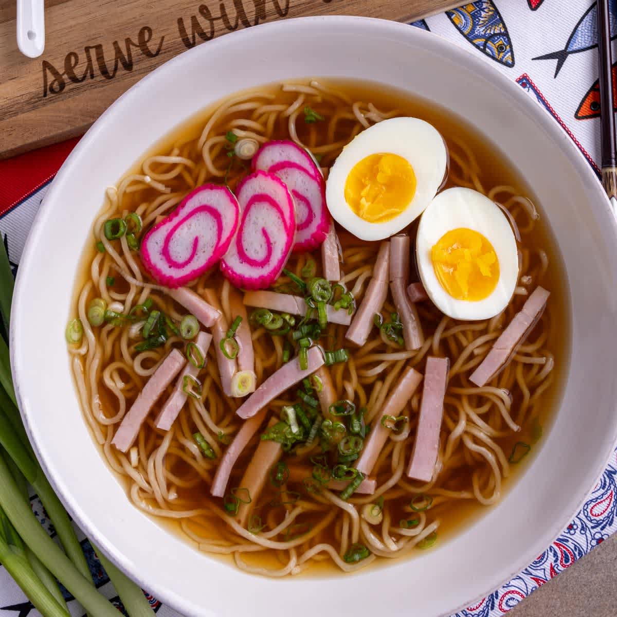 A bowl of traditional Hawaiian saimin noodle soup with fish cake, boiled egg, ham, and green onions, showcasing local comfort food