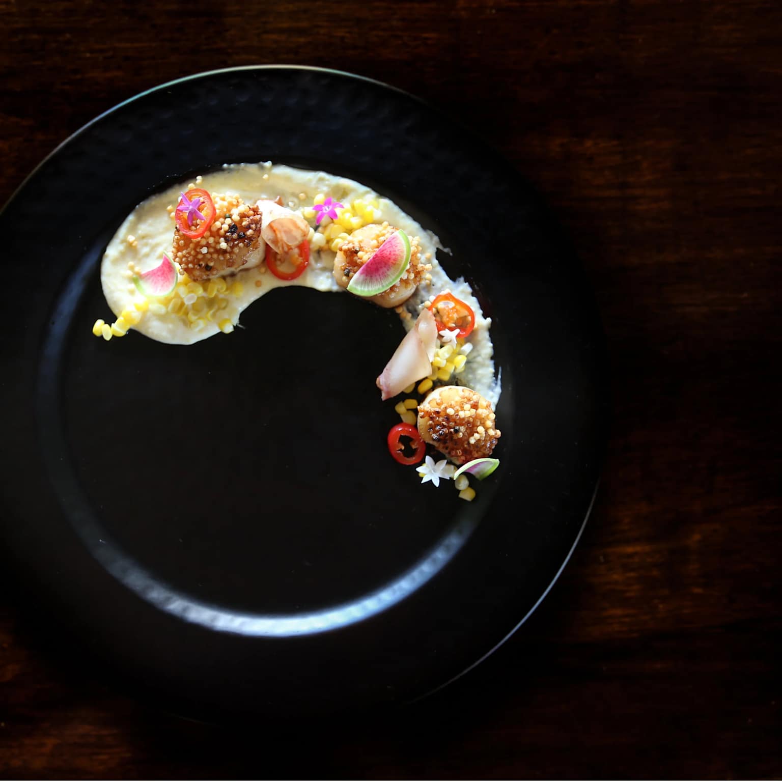Artfully plated seared scallops with vibrant garnishes on a black plate showcasing fine dining in Hawaii