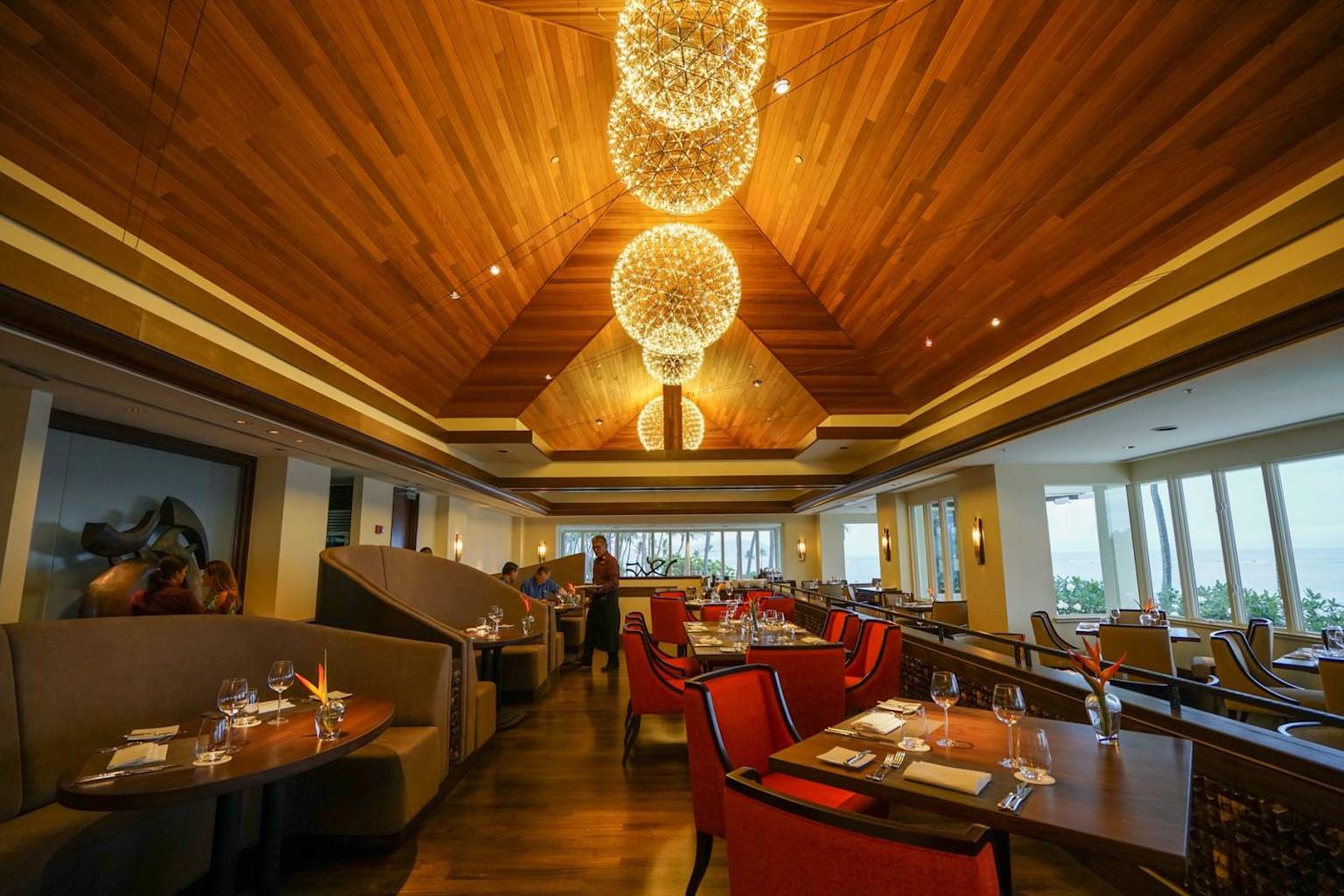 Interior of Hoku's at The Kahala Hotel & Resort showcasing elegant dining with warm wood tones and stunning chandeliers