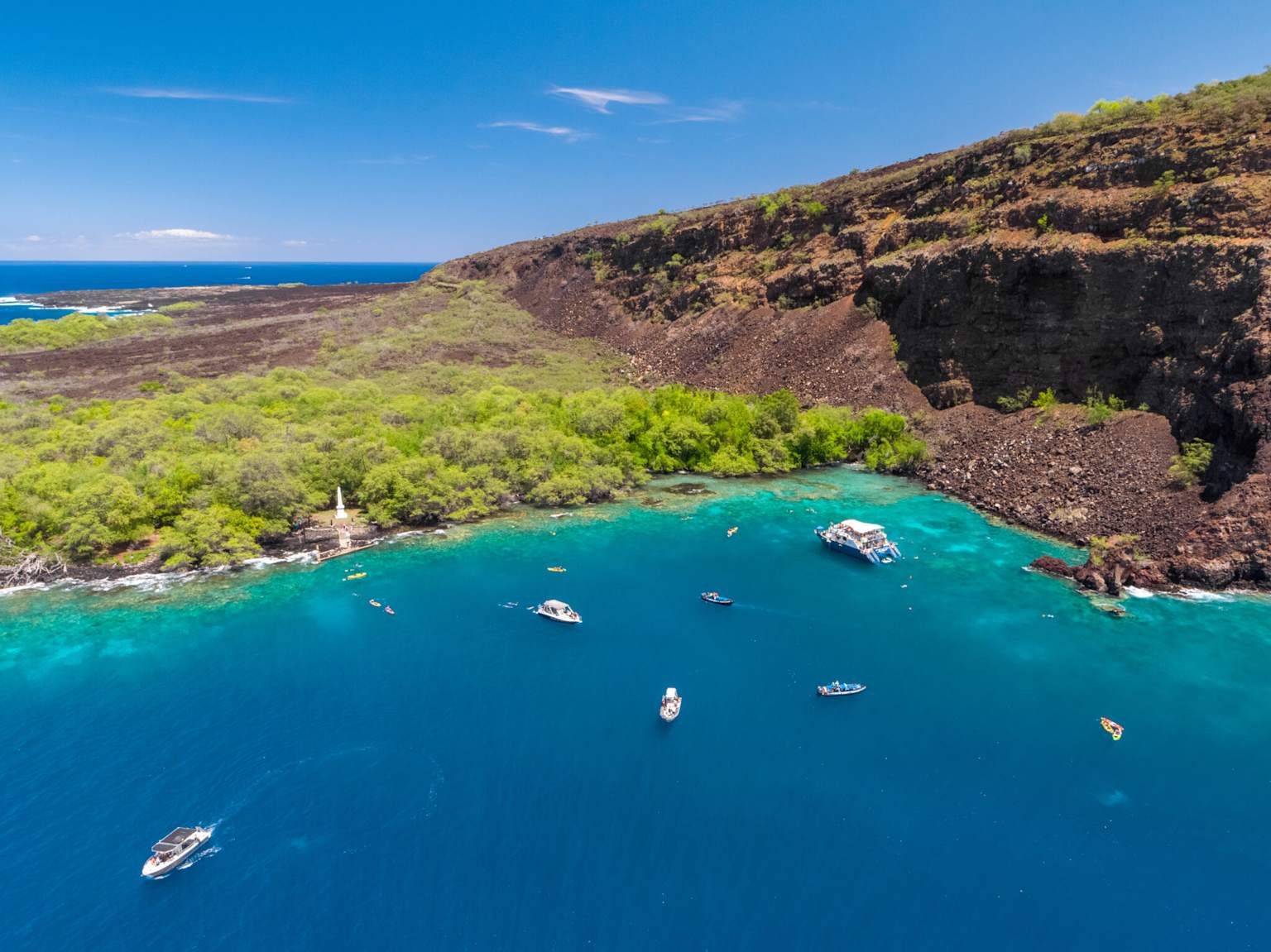 Aerial view of Kealakekua Bay showcasing boats and snorkelers in clear blue waters surrounded by volcanic cliffs and lush greenery, a top snorkeling spot in Hawaii