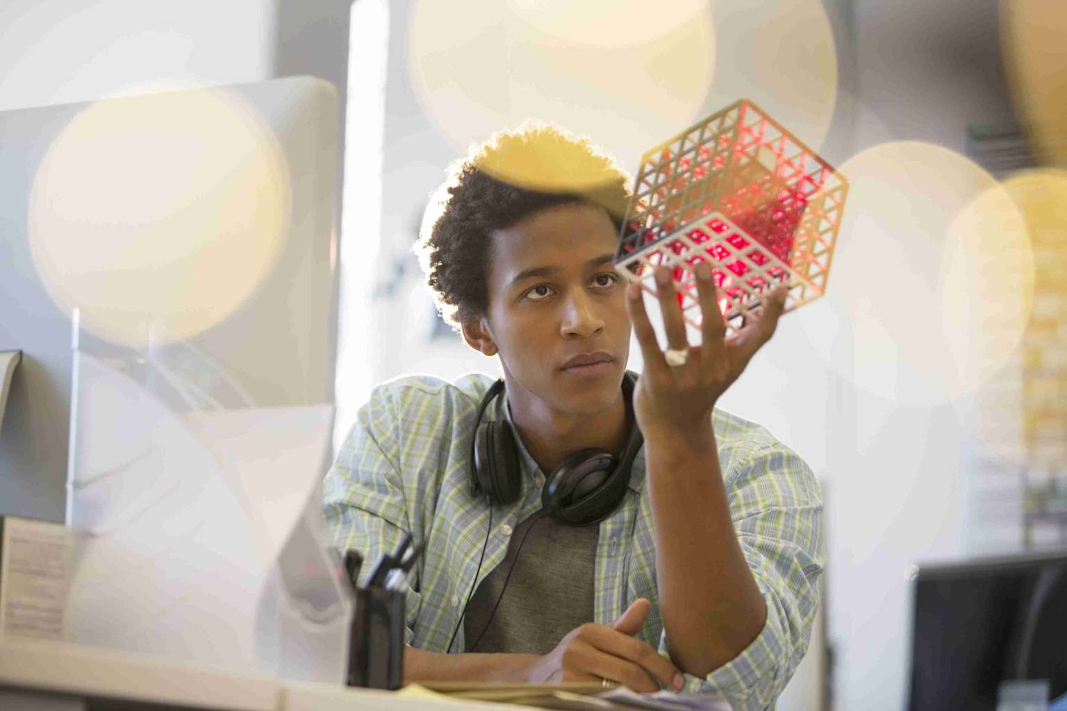 Person in a creative workspace holding a geometric object while wearing headphones, symbolizing deep focus and flow state