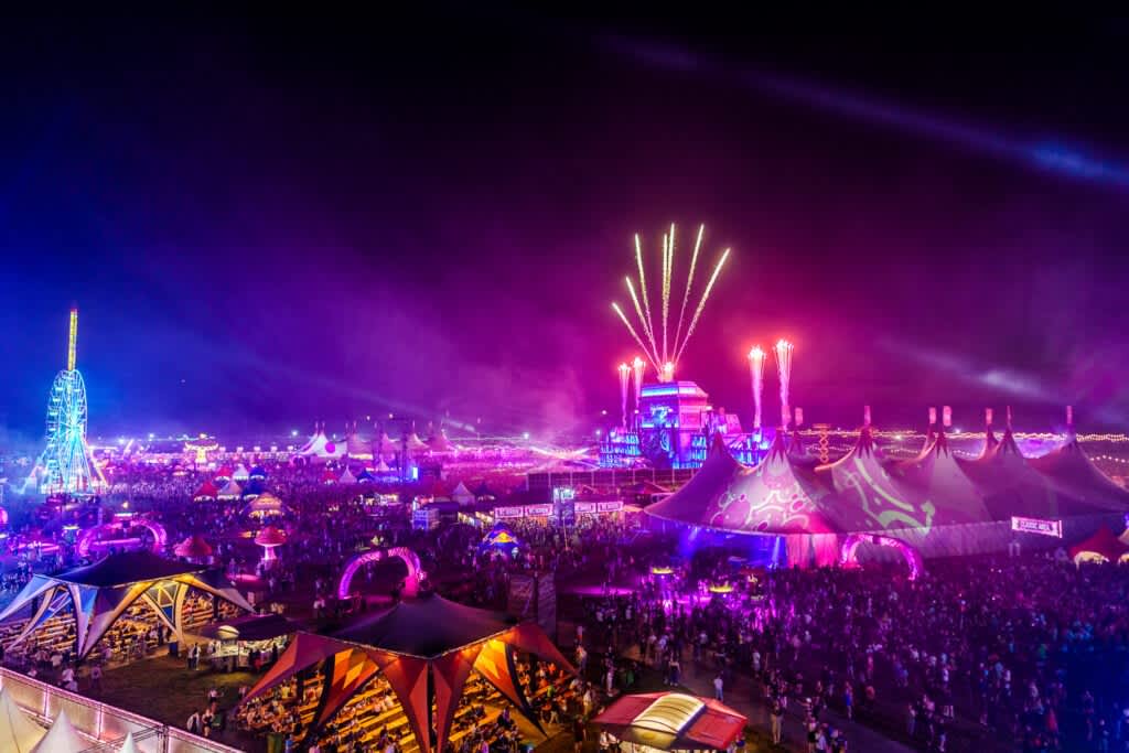 Airbeat One Festival at night with main stage, fireworks, ferris wheel, and large crowd under colorful lights