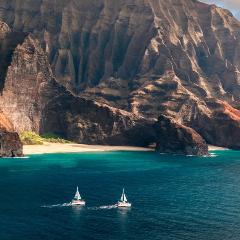 View of Na Pali Coast on Kauai with catamarans sailing near sandy beach and rugged cliffs