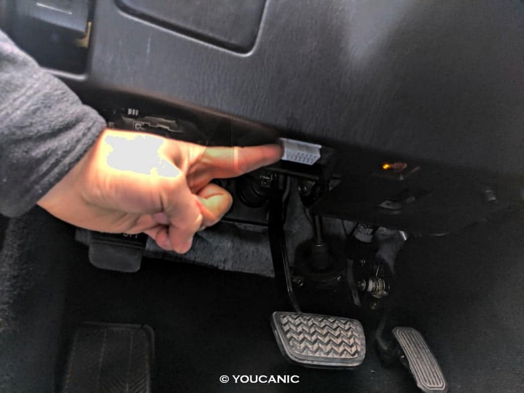 White OBD-II diagnostic port located under the car dashboard near the brake pedal for easy access