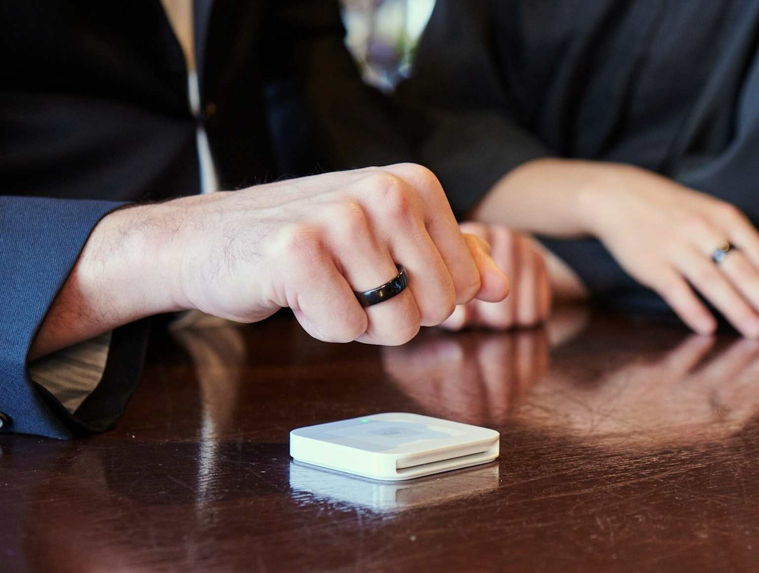 Two people using black smart rings for contactless payments with a payment terminal device on the table