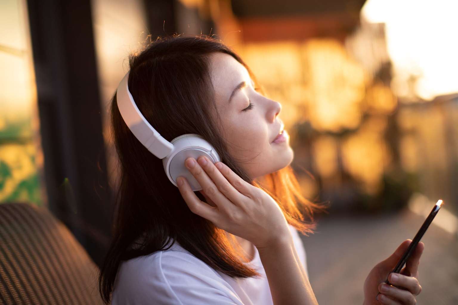 Young adult deeply focused while listening to music on headphones during sunset, illustrating concentration and creativity enhancement