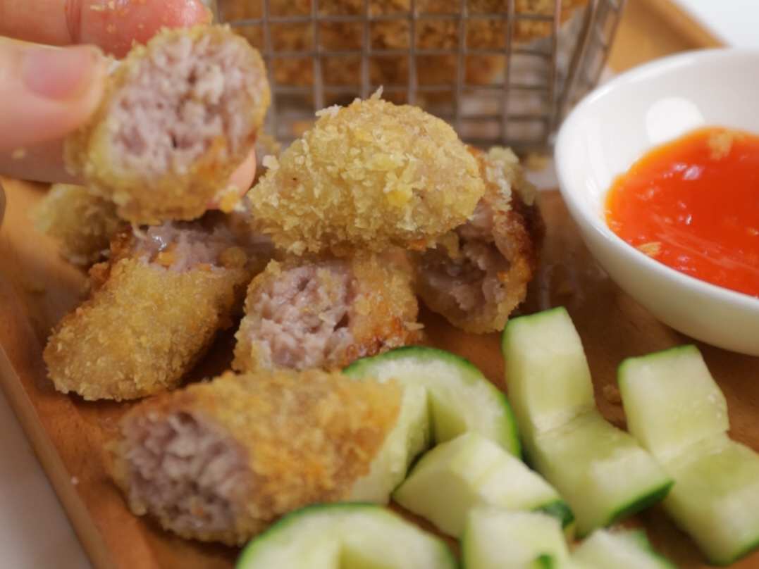 Close-up of nem chua rán (deep-fried fermented pork rolls) served with cucumber and chili dipping sauce, a popular Hanoi street food snack