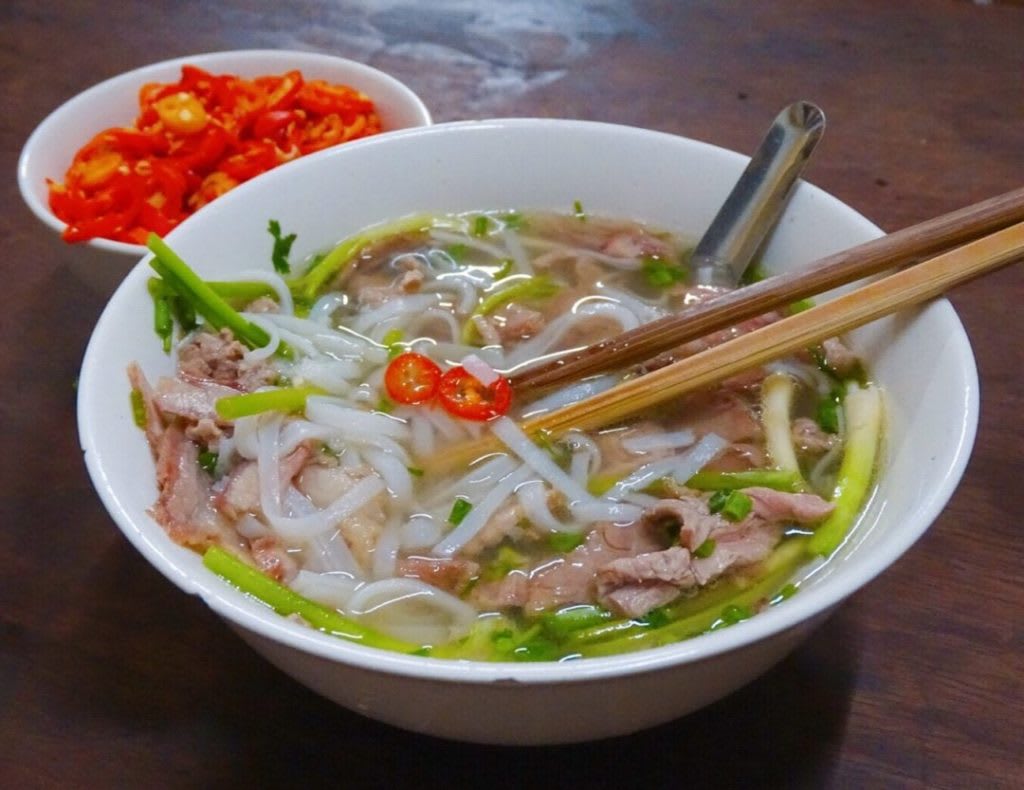 A bowl of traditional Hanoi pho with beef, noodles, herbs, and chili peppers ready to eat as a breakfast street food