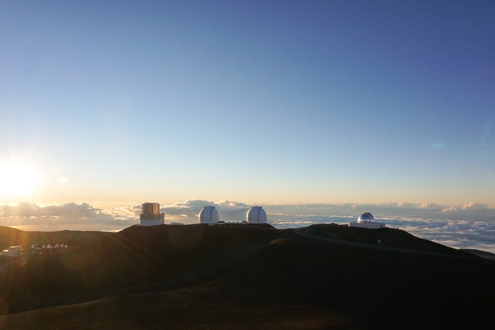 Mauna Kea summit observatories silhouetted at sunrise above clouds on Hawaii's Big Island