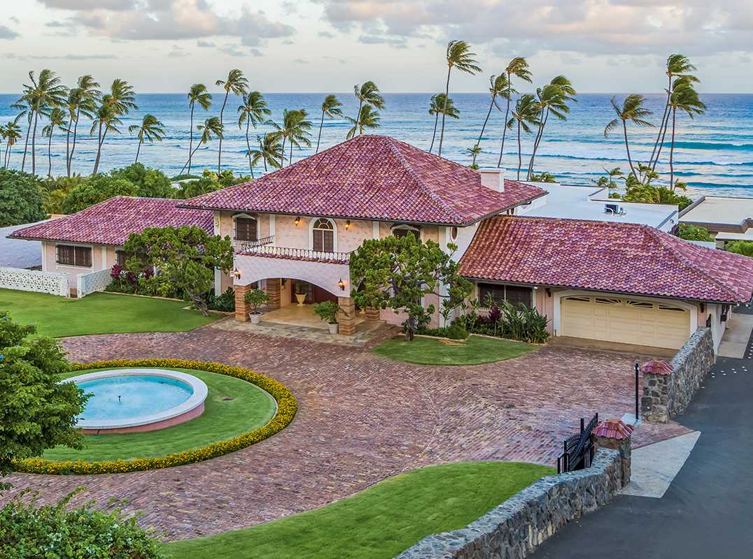 Luxury oceanfront estate with red-tiled roof and palm trees in a Hawaii neighborhood near Diamond Head