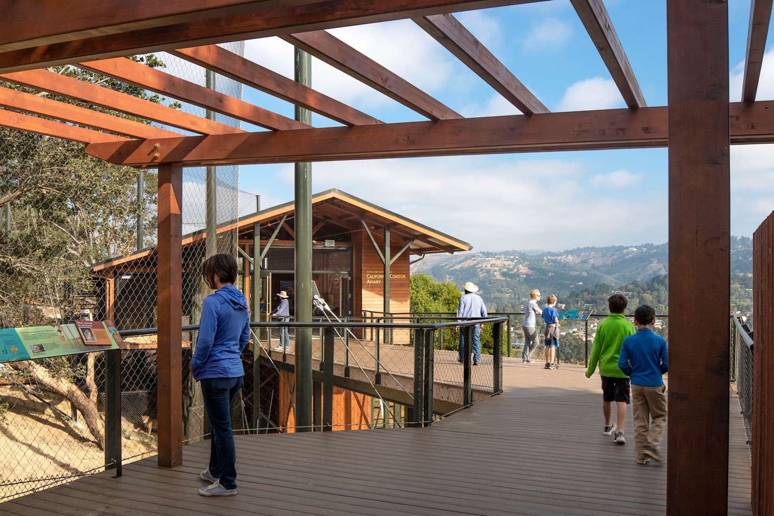 Visitors explore the California Trail boardwalk and condor aviary at the Oakland Zoo on a clear day with scenic mountain views