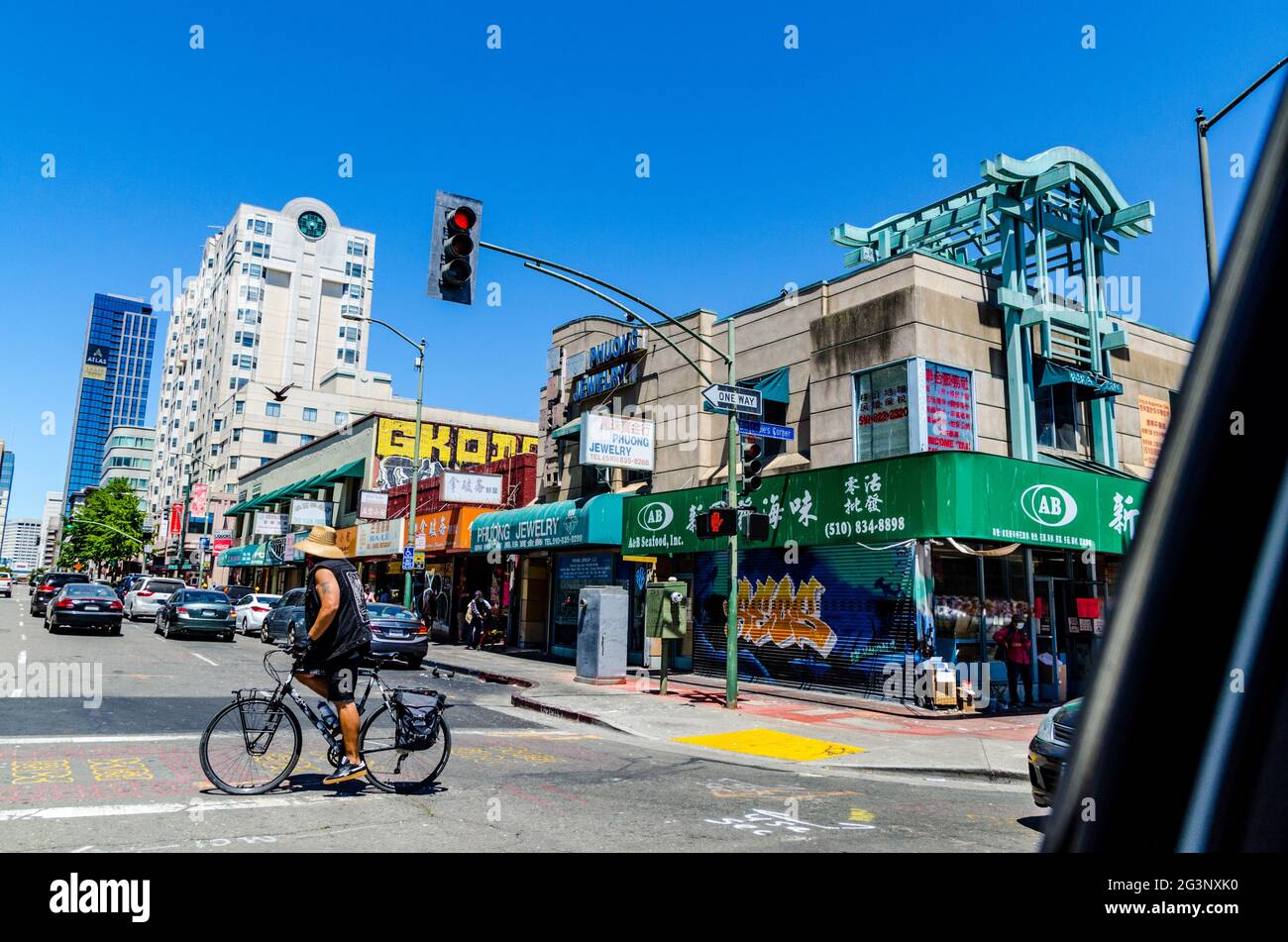 Street scene in Oakland Chinatown showing local shops, a cyclist crossing the street, and distinct architectural elements on a sunny day