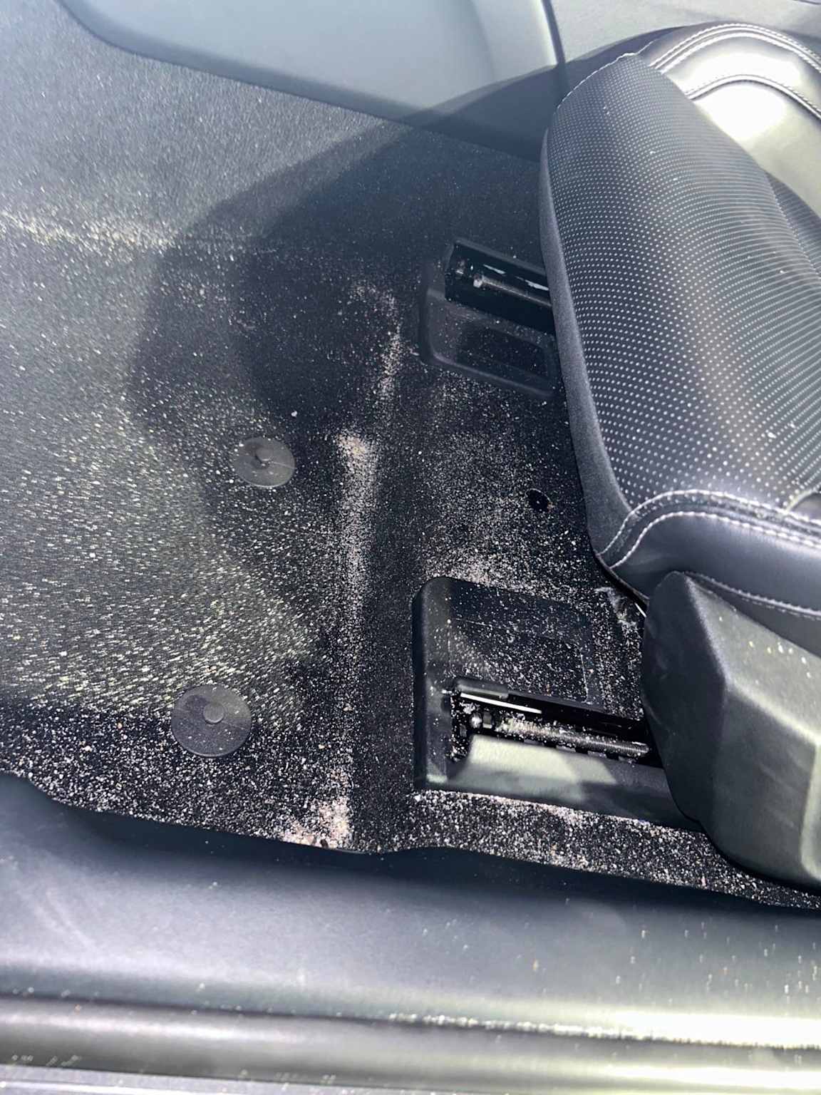 Sand scattered on the interior carpet of a rental car near the front seat, illustrating a common trigger for cleaning fees in beach destinations like Hawaii