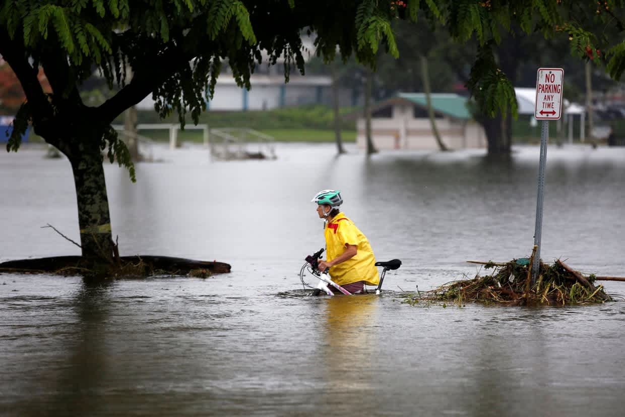 A person wades through waist-deep floodwaters in Hawaii during a heavy storm, highlighting the wet season's unexpected challenges
