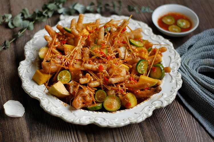 Spicy Thai-style chicken feet with calamansi slices garnished on a decorative white plate