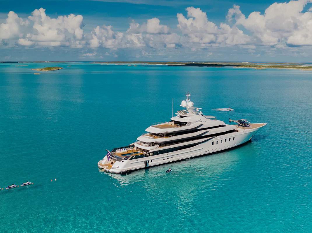 Luxury yacht with helicopter and jet skis in turquoise waters of the Bahamas, illustrating upscale yacht charter experiences