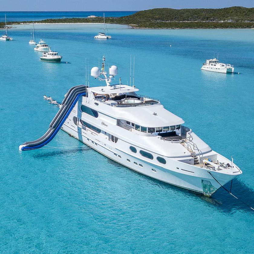 Luxury white yacht with inflatable slide anchored in clear turquoise Caribbean waters near a lush island