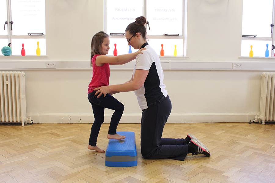 A personal trainer supports a child with a disability during a step-up exercise, highlighting the benefits of tailored physical activity and hands-on guidance