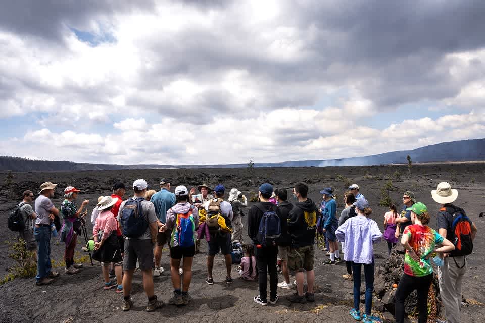 A multi-generational group enjoys an educational tour on the volcanic terrain at Hawai'i Volcanoes National Park, showcasing an engaging family activity suitable for ages 5 to 85