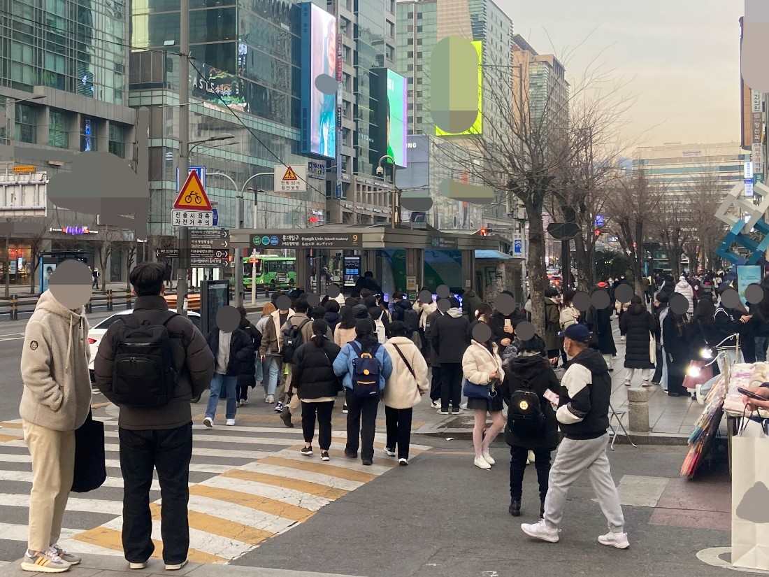 Pedestrians crossing near Hongdae Entrance Exit 9 in a bustling Seoul street scene.