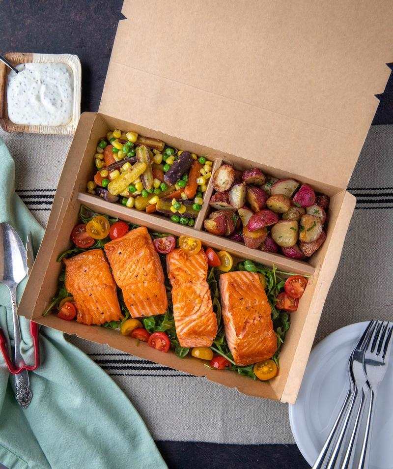 Sustainable meal delivery using eco-friendly cardboard bento box with salmon, vegetables, and potatoes.