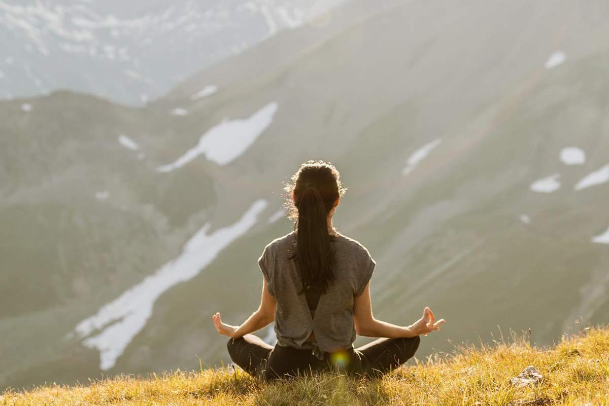 A person meditates amid peaceful mountain scenery, embodying mindful and slow travel relaxation