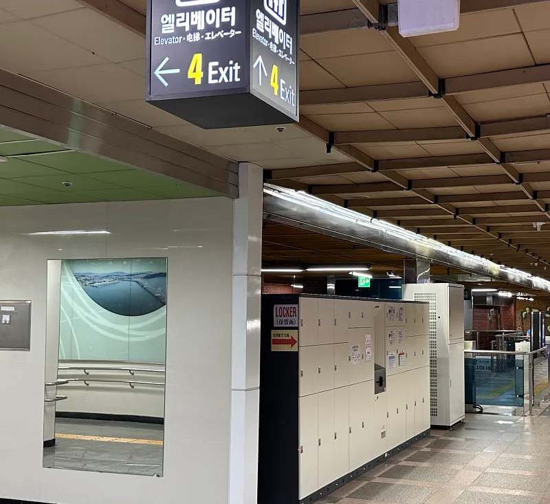 Signage inside Busan Station showing directions to elevator and Exit 4 alongside baggage lockers.