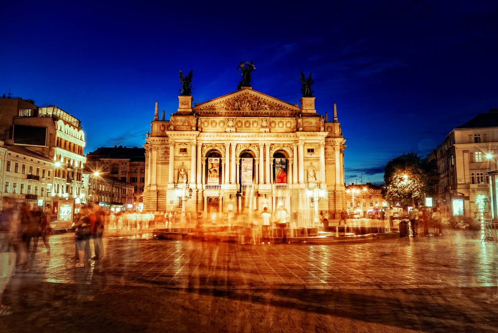 The Lviv Opera House illuminated in the evening, showcasing its neo-renaissance architecture and lively surroundings