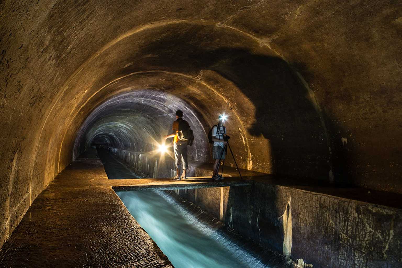 Exploring the arched underground tunnel in Lviv's subterranean river system with flashlights and camera setup