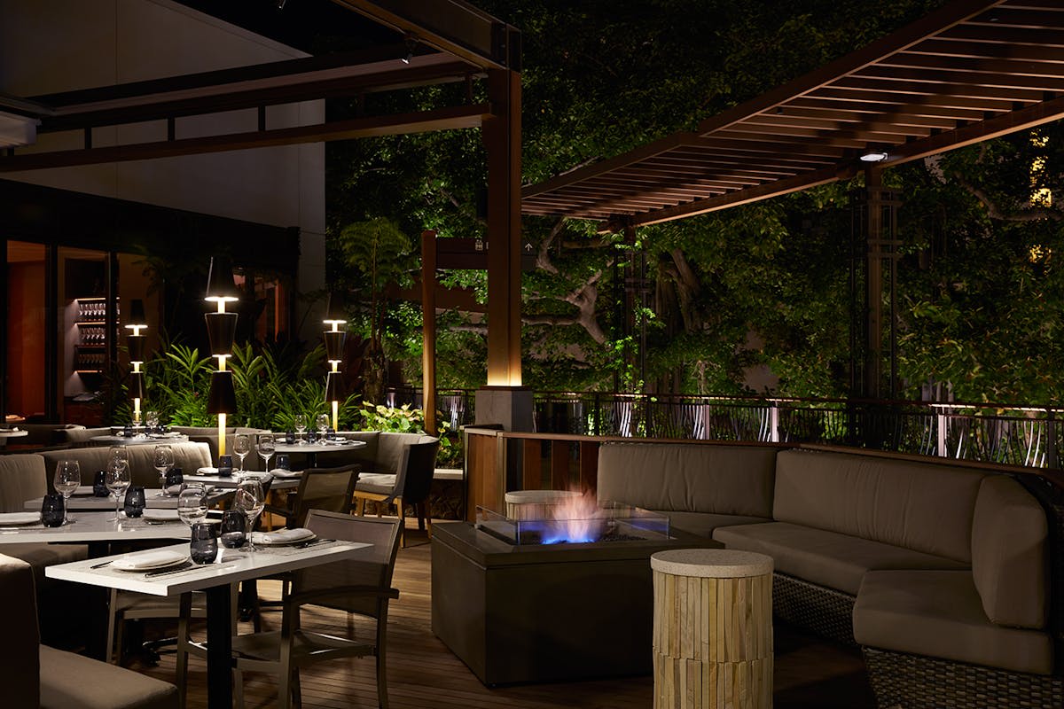 Outdoor nighttime seating at STRIPSTEAK by Michael Mina in Waikiki with ambient lighting and a fire pit creating a warm dining atmosphere