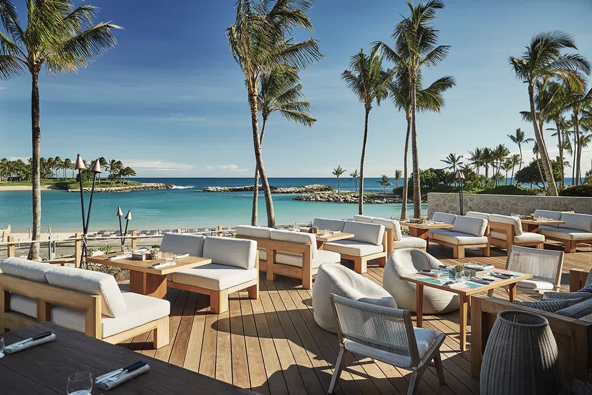 Outdoor dining area with ocean views and palm trees in a tropical beach setting, exemplifying Hawaii's beachfront restaurant ambiance