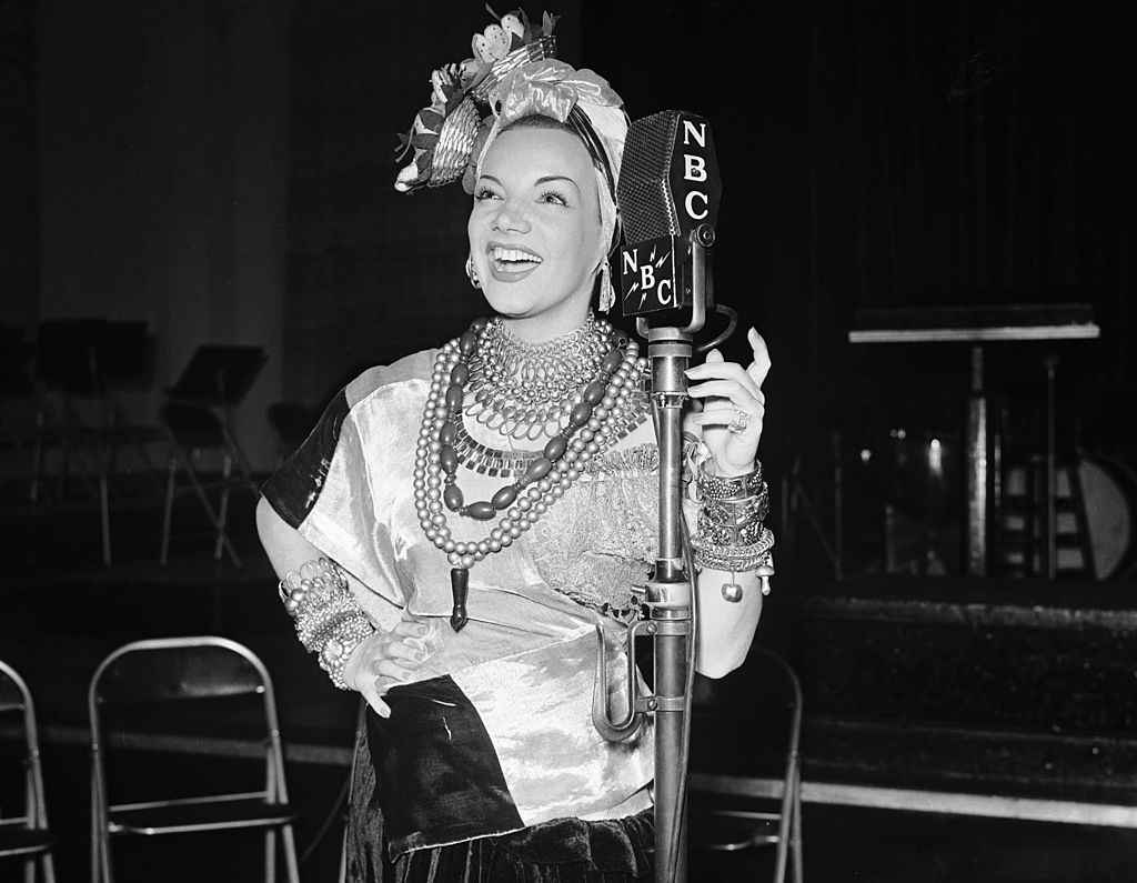 Carmen Miranda in her iconic fruit-laden headdress and jewelry performing beside an NBC radio microphone in the 1930s.