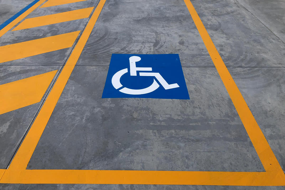 Parking space reserved for disabled individuals marked with yellow lines and the international wheelchair symbol on concrete ground