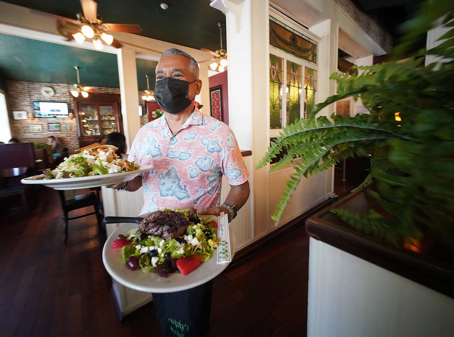 A server in a Hawaiian restaurant carrying plates of fresh salads with grilled steak and fruit