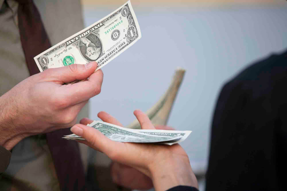 A person handing over a one-dollar bill as a tip in a restaurant setting