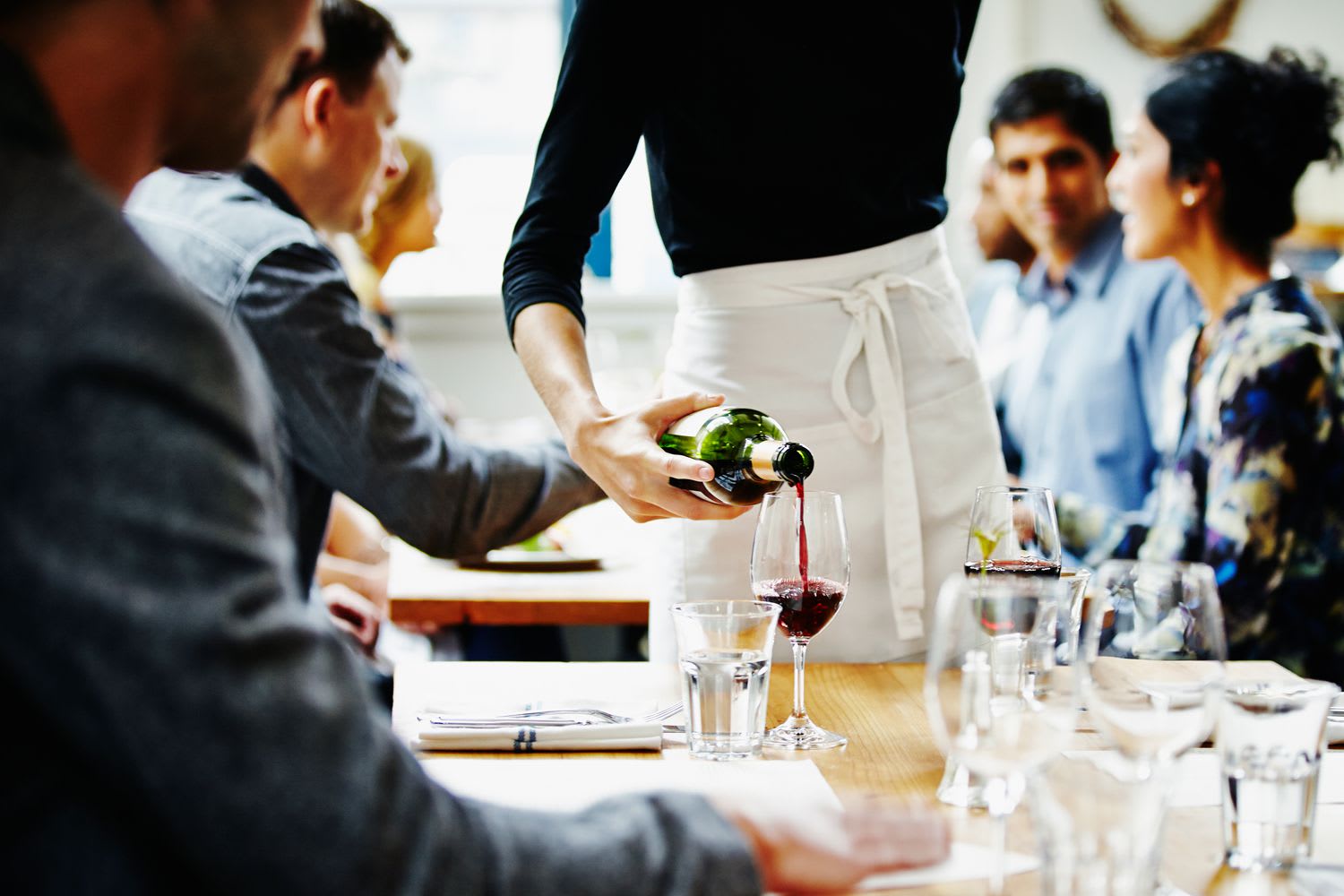 Server pouring red wine into a glass at a neatly set restaurant table