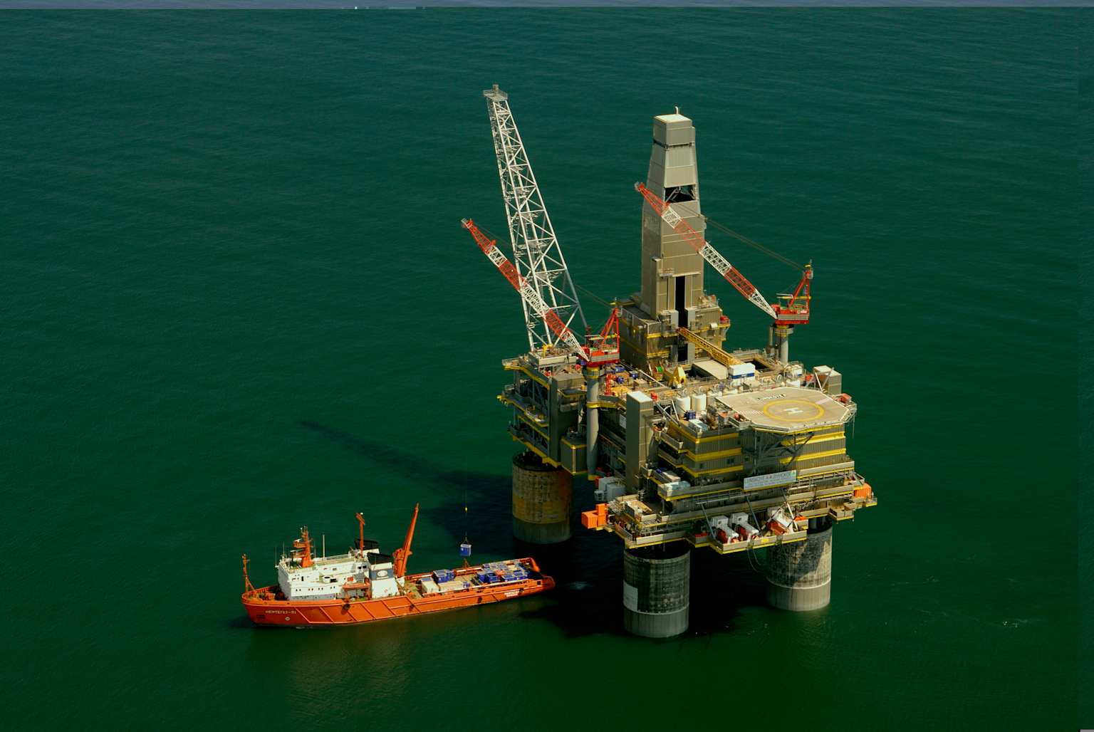 An offshore oil drilling platform with cranes and a supply ship in the ocean