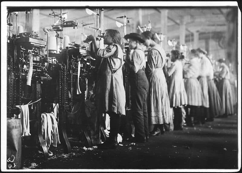 Young female factory workers operating industrial machines during the Industrial Revolution, illustrating early capitalist labor conditions.