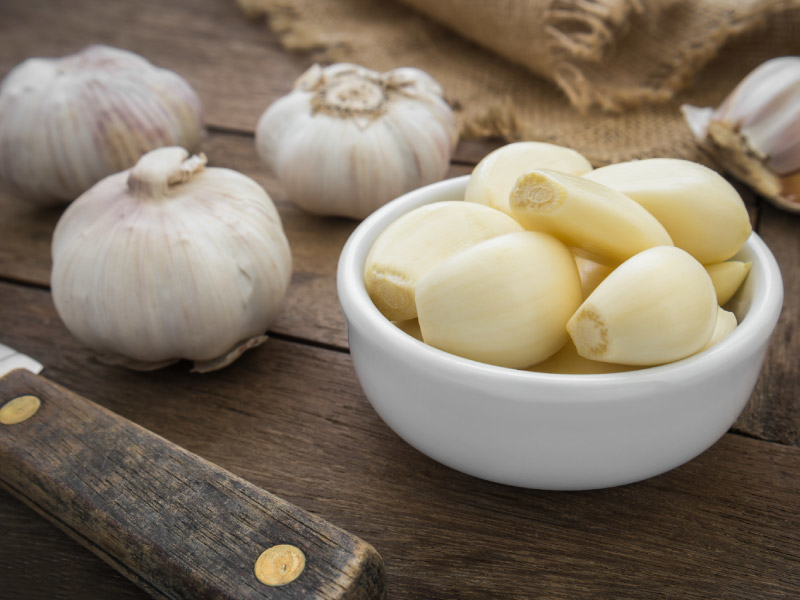 Fresh whole garlic bulbs and peeled cloves displayed on a wooden surface, illustrating raw garlic typically used for health benefits