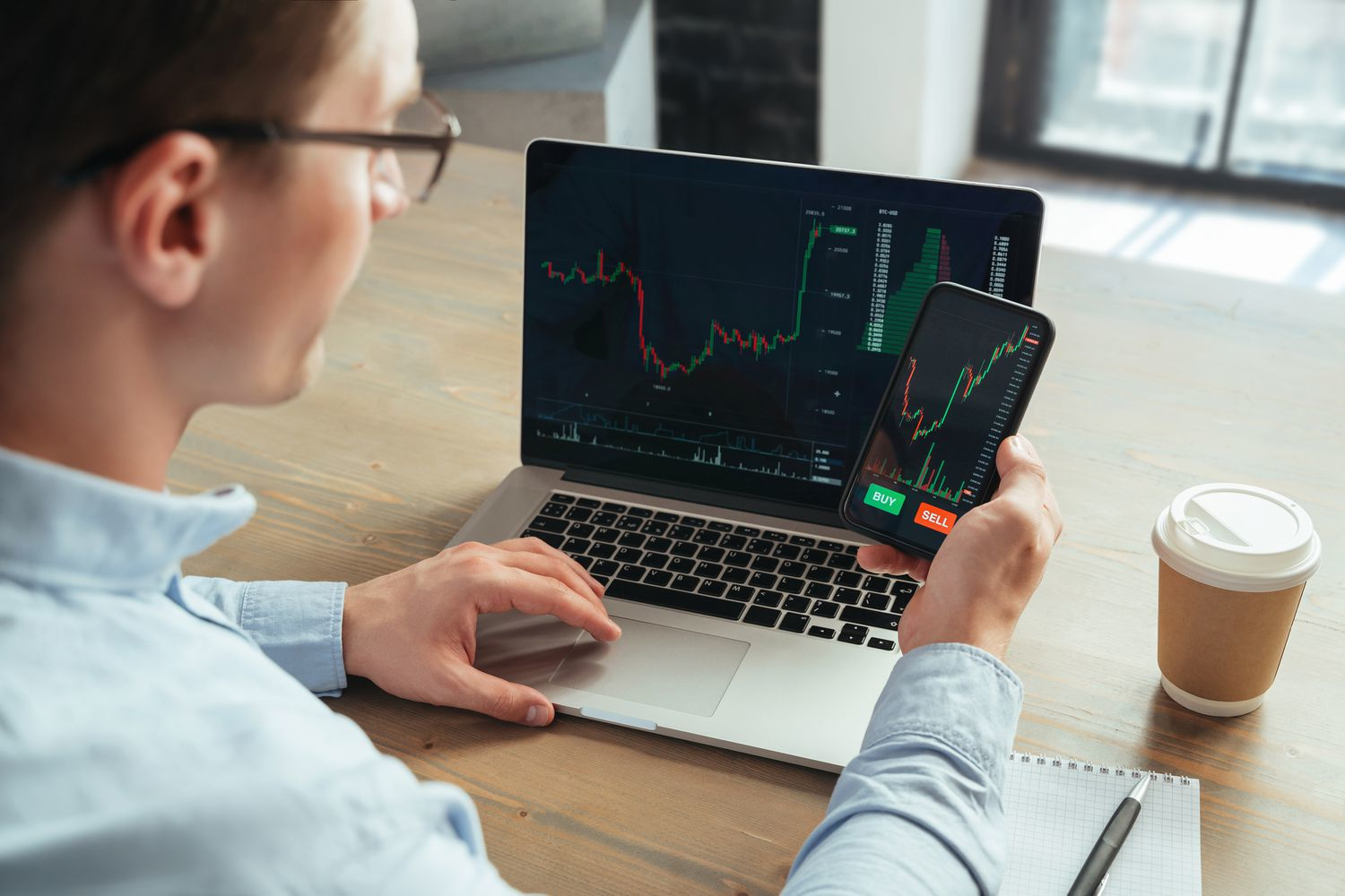 Trader monitoring cryptocurrency price charts on laptop and smartphone with buy and sell options