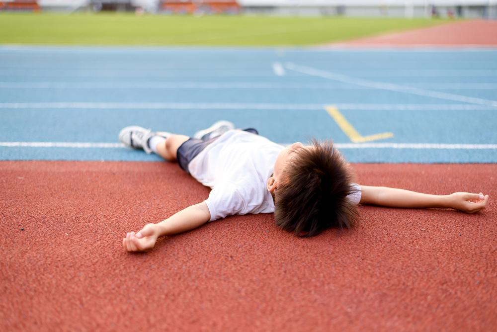 A young athlete lying exhausted on a running track after intense physical activity, illustrating the importance of rest and recovery