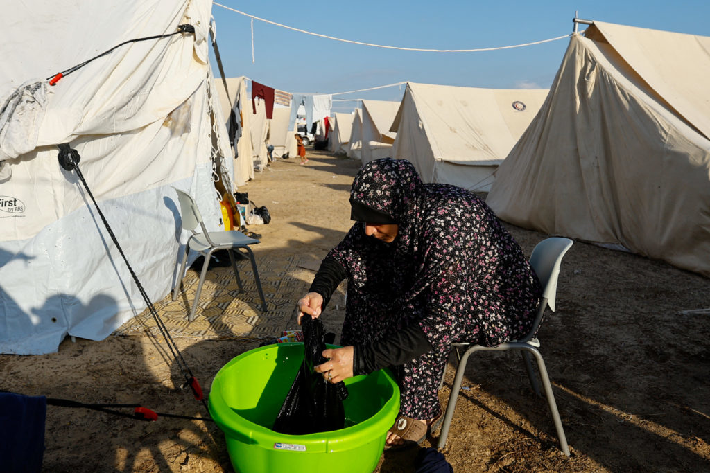 A woman washes clothes at a tent camp for displaced Palestinians in southern Gaza, highlighting daily life in a refugee camp