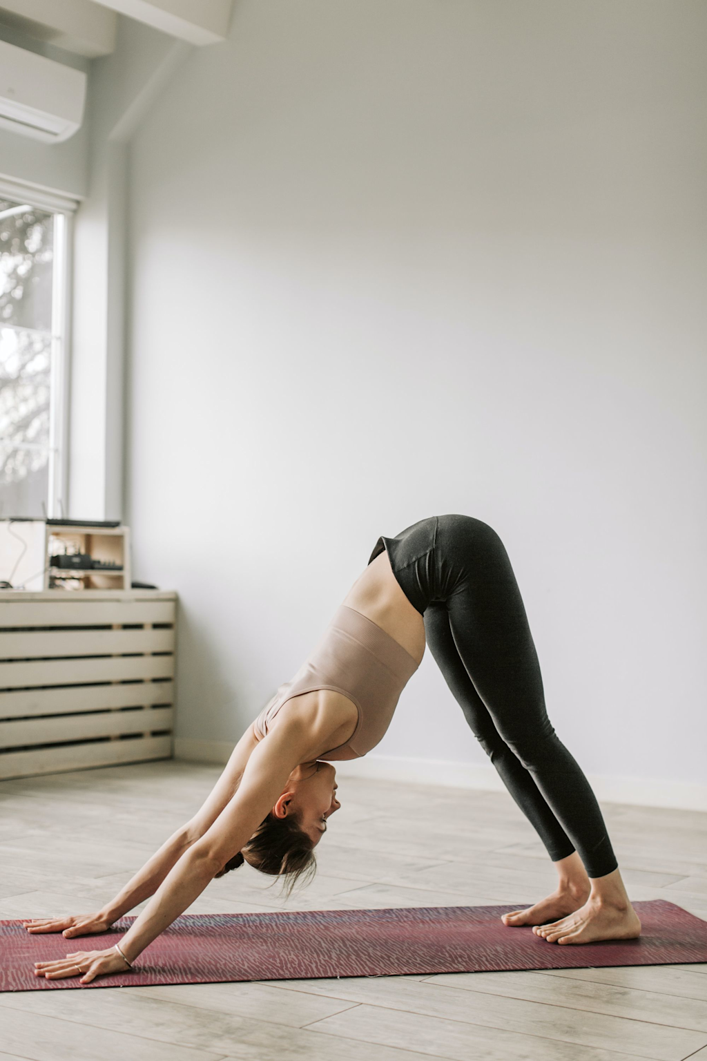 A woman performing the downward dog yoga pose indoors, demonstrating a beginner-level hatha yoga posture